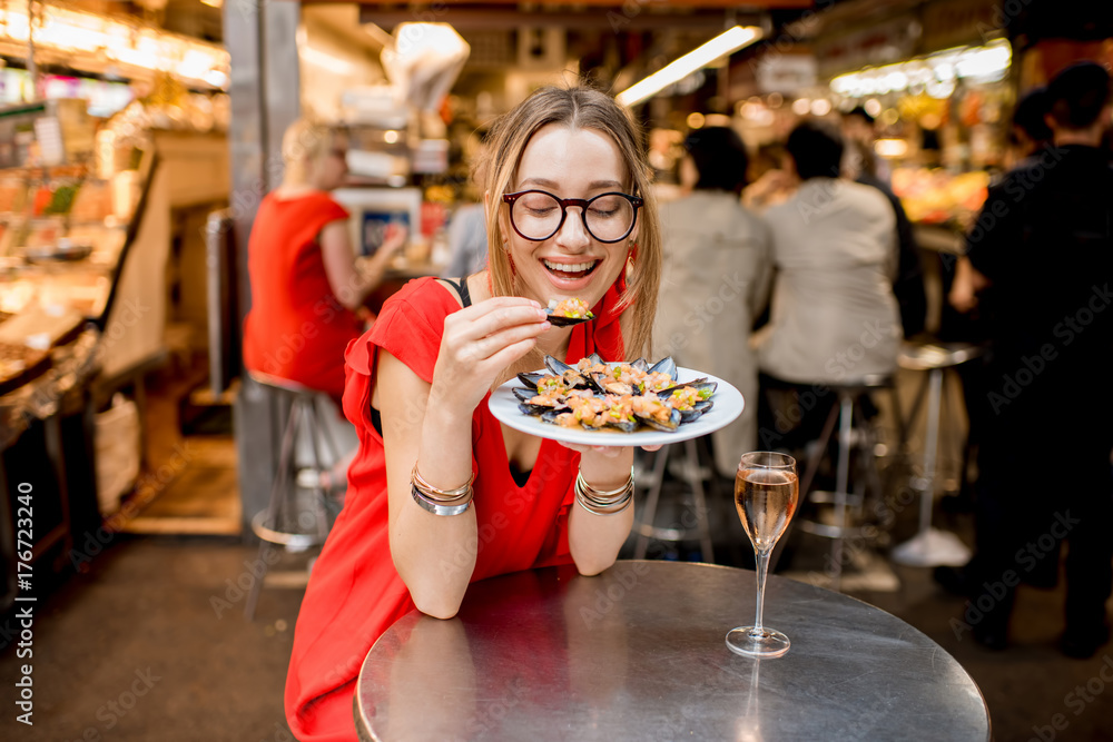 一位身穿红色连衣裙的年轻女士坐在食品市场上与贻贝和玫瑰酒共进午餐