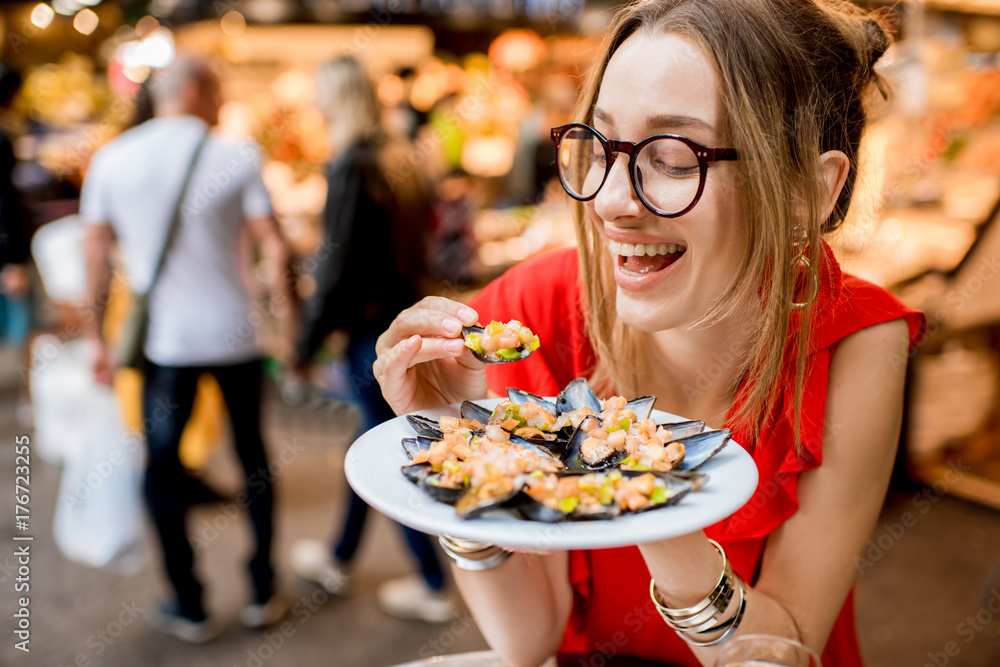 一位身穿红色连衣裙的年轻女子坐在食品市场上与贻贝和玫瑰酒共进午餐