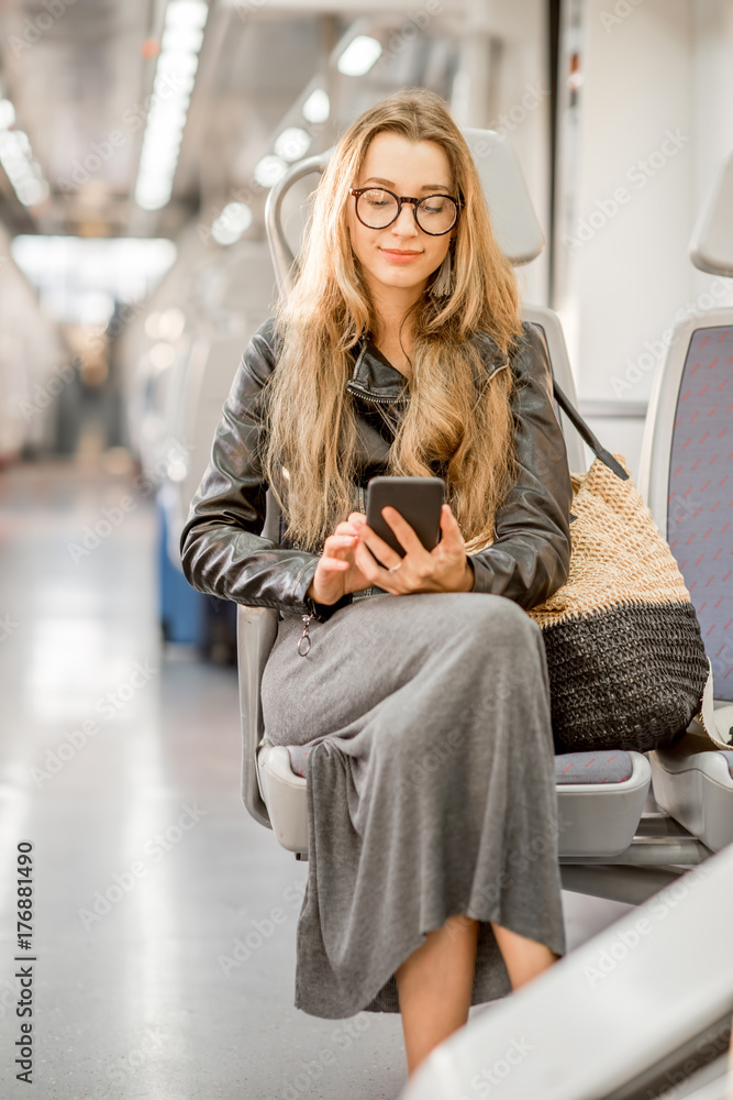一位年轻女商人拿着智能手机坐在现代火车上的生活方式画像