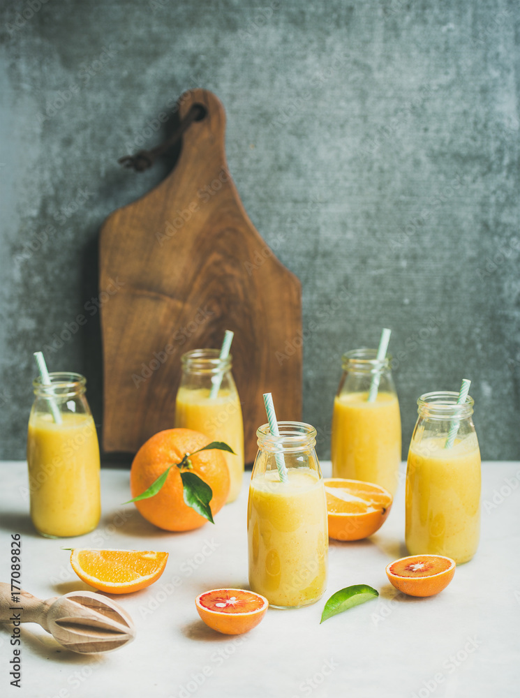 健康的黄色奶昔，配柑橘类水果，装在浅色大理石桌子上的瓶子里的生姜，木板和