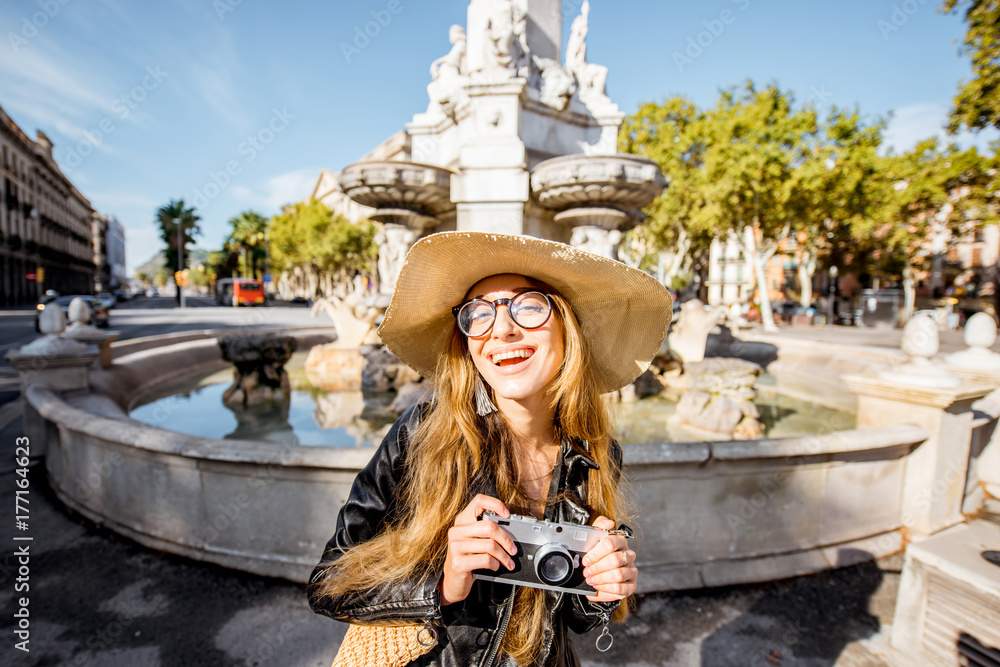 一位年轻女游客的肖像，她拿着相机站在巴塞罗那市的喷泉附近