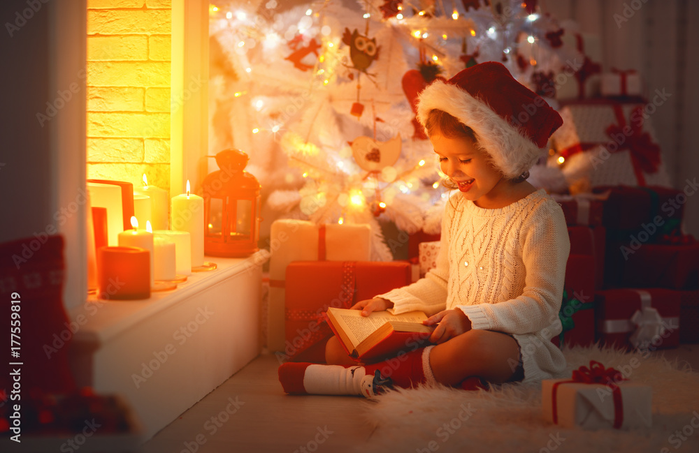圣诞节快乐的小女孩在家里的壁炉旁看书。