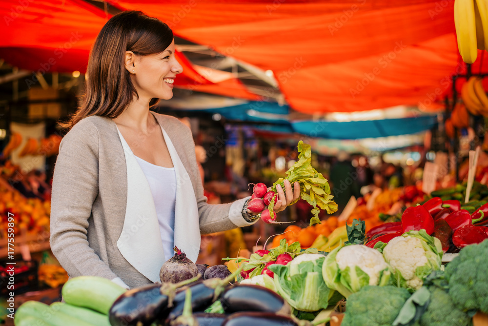 年轻女子在市场买蔬菜。