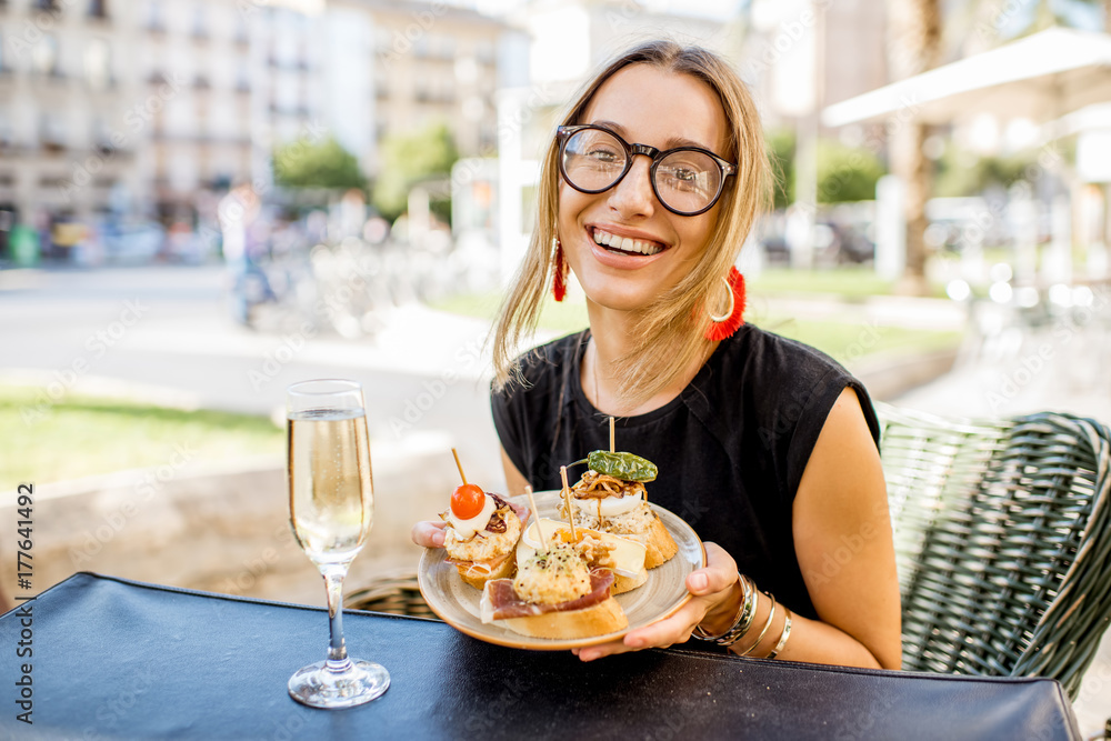 一位年轻女士正在享用美味的开胃菜，配以西班牙传统小吃pinchos和一杯葡萄酒