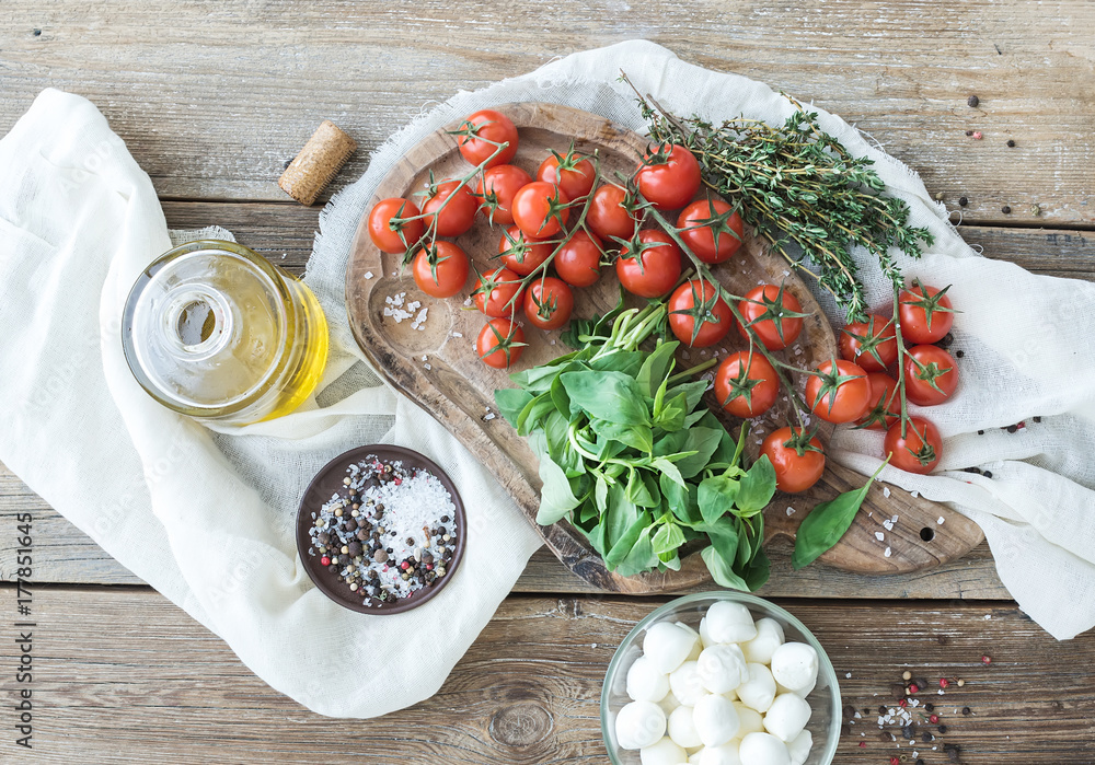罗勒、樱桃番茄、马苏里拉奶酪、橄榄油、盐、香料放在古老的木板上
