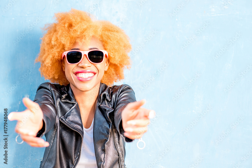 Lifestyle portrait of an african woman in leather jacket standing on the blue wall background