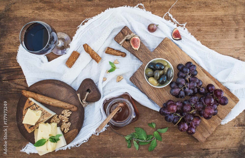 一杯红酒、奶酪板、葡萄、橄榄、蜂蜜、核桃和面包棒放在乡村的木头上