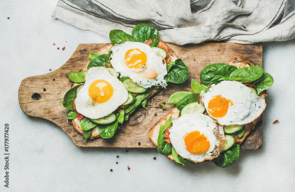 健康的早餐三明治。在木板上烤面包，配煎蛋和新鲜蔬菜