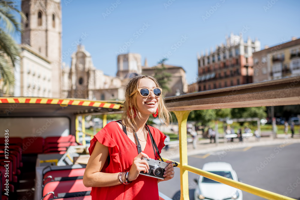 年轻快乐的女游客，穿着红色连衣裙，在巴伦西亚市乘坐开放式旅游巴士游览。