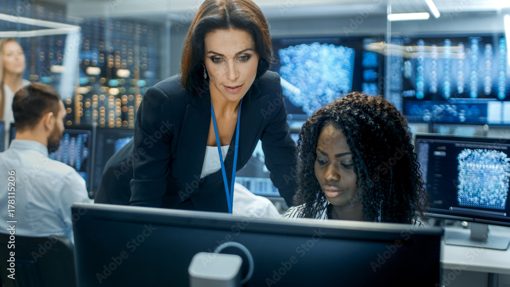 女组长咨询年轻的计算机工程师。她们在神经网络上拥挤的办公室工作