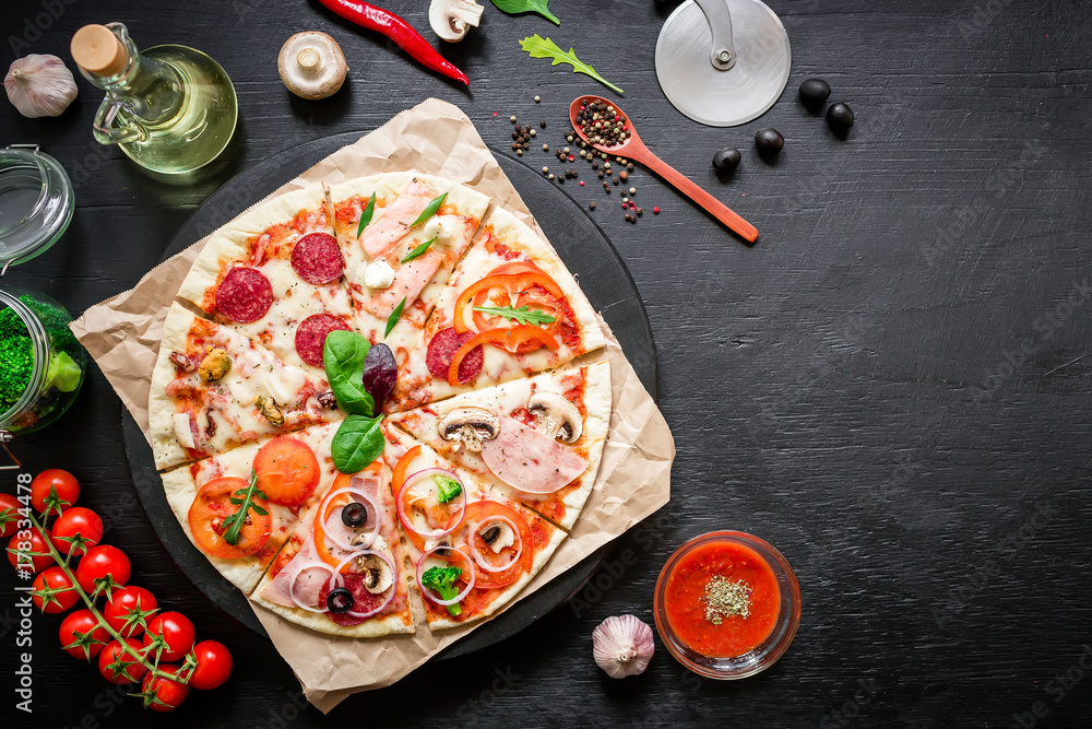 Pizza with ingredients, spices, oil and vegetables on dark table. Flat lay, top view.