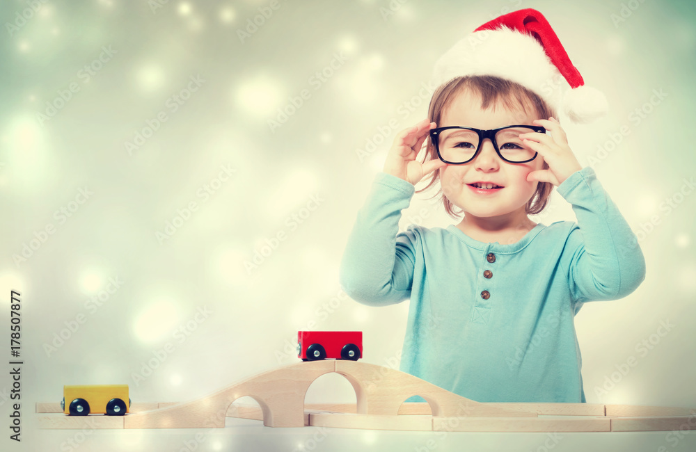 快乐的蹒跚学步的女孩，戴着圣诞老人的帽子和眼镜，玩她的玩具
