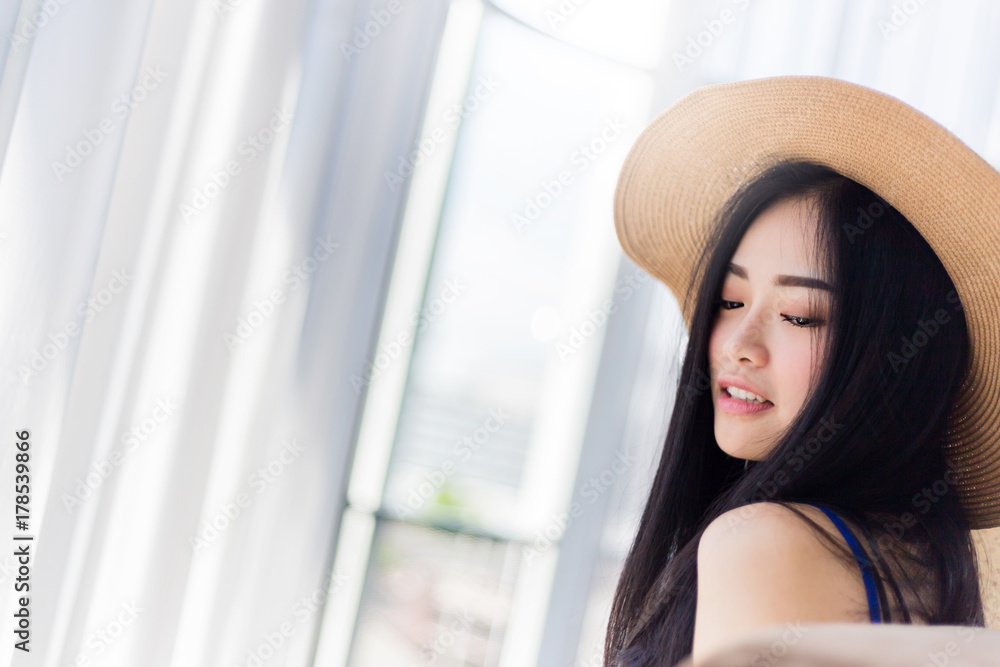 可爱的亚洲女孩，穿着夏装，戴着帽子，以白色房间为背景，摆出放松的姿势