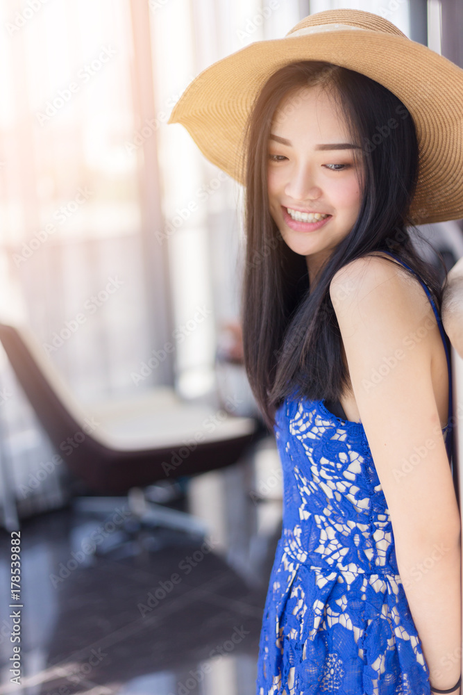 可爱的亚洲女孩，搭配夏季连衣裙和帽子，以白色房间为背景，摆出放松的姿势
