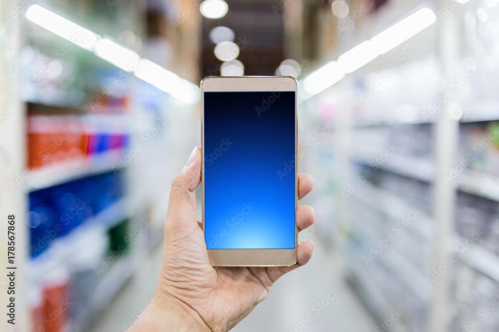 手拿智能手机，超市货架模糊图像背景
