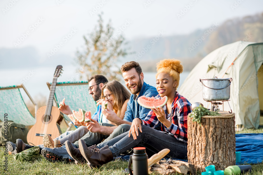 Multi ethnic group of friends having a picnic, eating watermelon during the outdoor recreation with 
