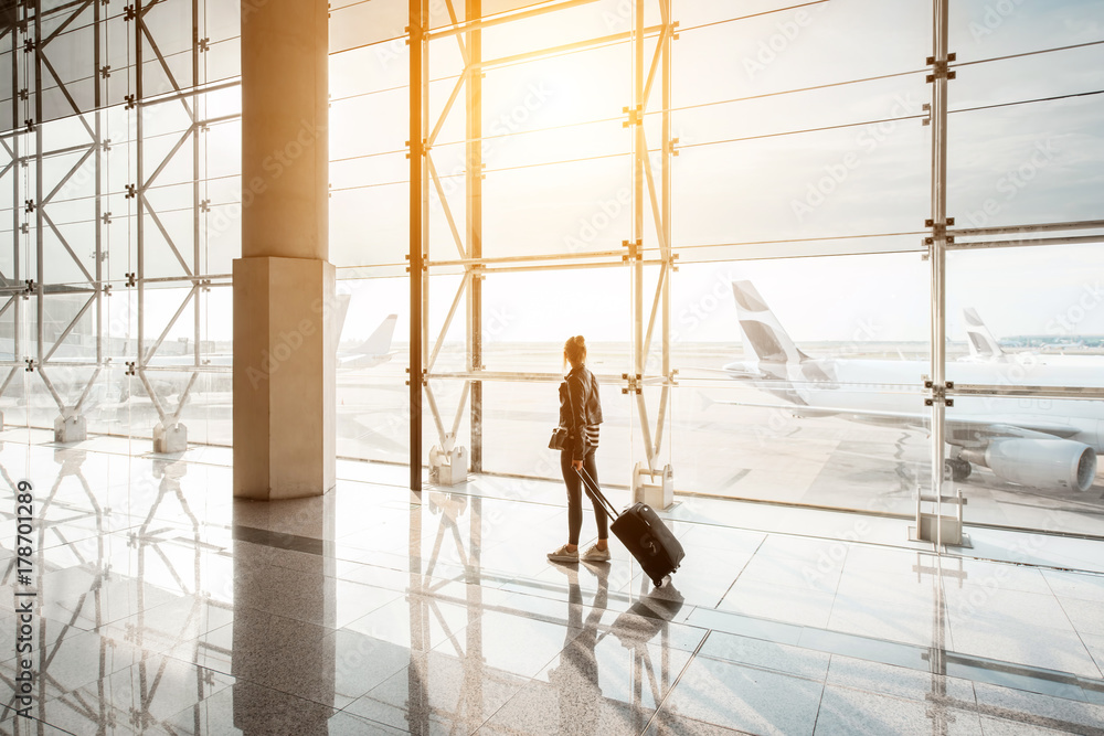 日落时分，在候机大厅，一名女子提着行李箱走在机场的窗户上。