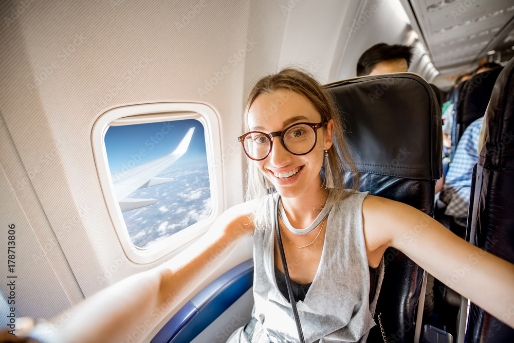 年轻快乐的女人在飞行中坐在靠近窗户的飞机座椅上自拍