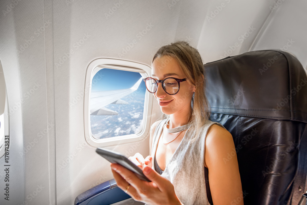 在空中飞行时，一名年轻女子拿着电话坐在靠近窗户的飞机座位上
