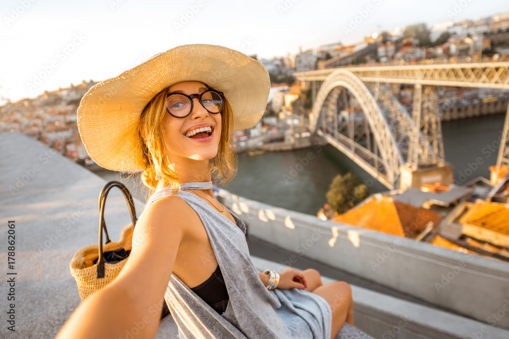 世纪年代，戴着太阳帽的年轻女游客在美丽的城市景观背景下自拍