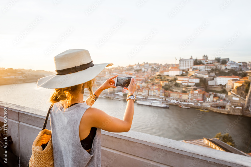 年轻女性游客用手机拍摄河边古镇的美丽风景