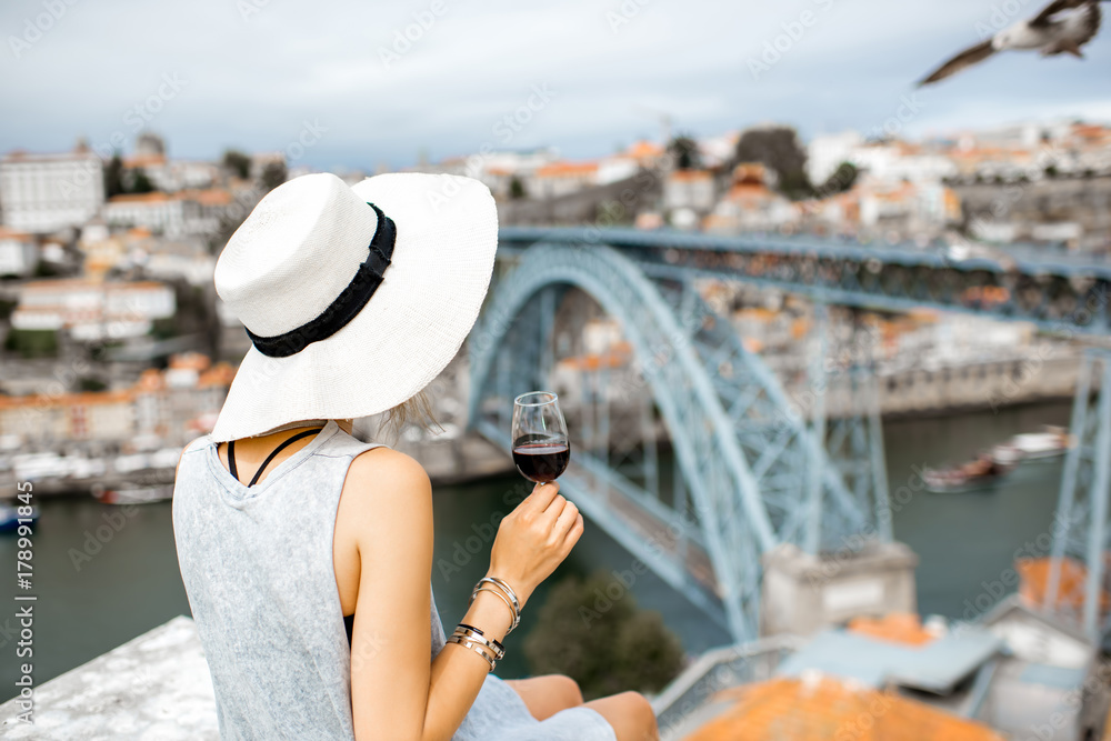 年轻的女游客拿着一杯波尔图葡萄酒坐在露台上，可以欣赏到波尔图的壮丽城市景观
