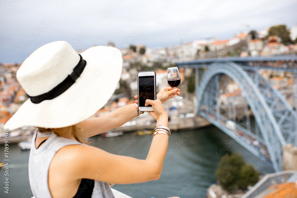 年轻的女游客坐在露台上拍摄一杯波尔图葡萄酒，城市景观优美