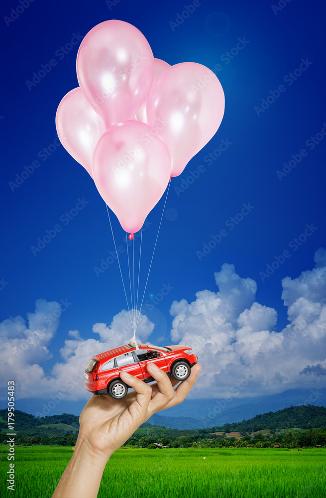 红色汽车在手，女人挂在蓝天上的许多气球上。汽车资产概念