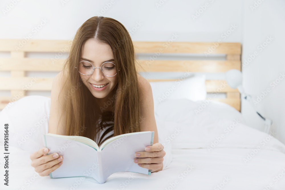 女孩躺在床上看书，趴在地上微笑，在家里度过一个悠闲的日子。