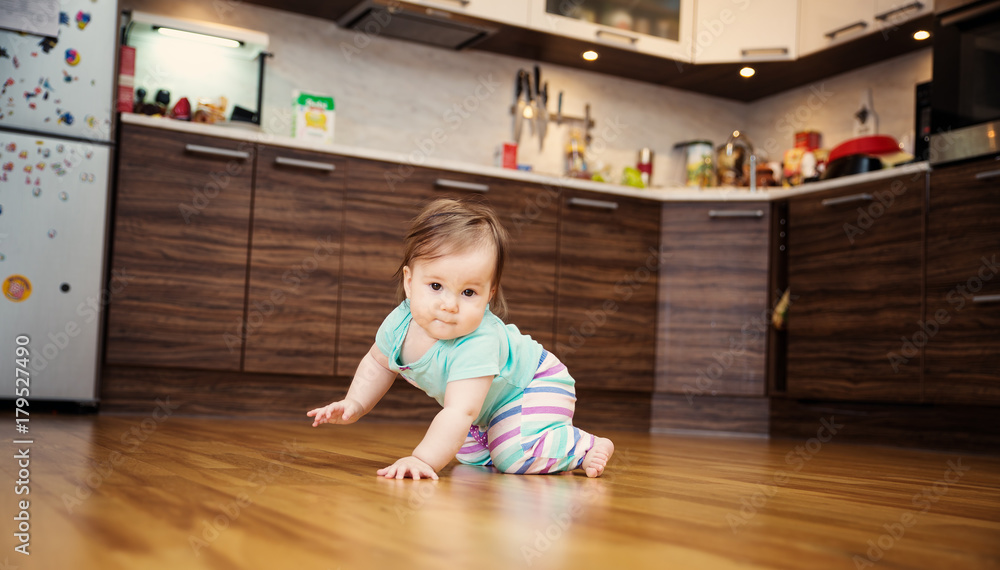 可爱的微笑小女婴在厨房的地板上爬行。家里有七个月大的婴儿