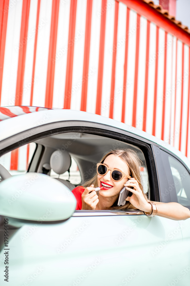夏天，一名年轻女子坐在车旁的条纹墙背景上画嘴唇