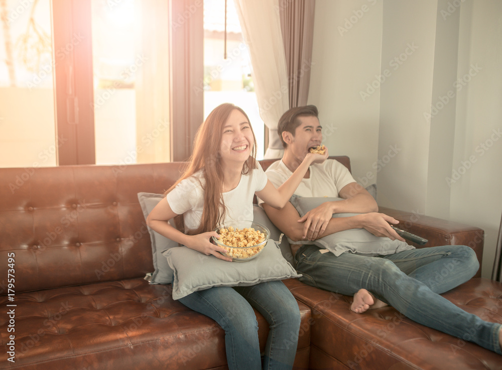 年轻夫妇在公寓里放松，躺在沙发上，看电影，吃爆米花。L