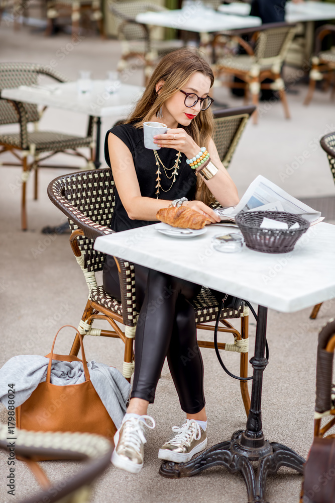一位年轻女士坐在户外典型的法式咖啡馆吃早餐，配咖啡和羊角面包