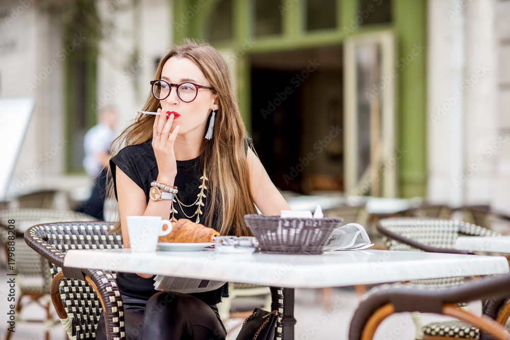 Young woman smoking a cigarette while having a breakfast outdoors at the typical french cafe terrace