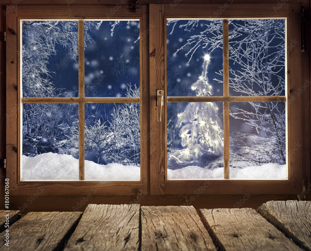 Blick aus einer Holzhütte auf einen Winterwald mit Weihnachtsbaum am Abend