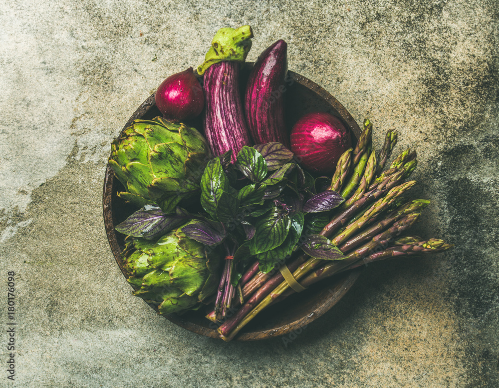 Flat-lay of green and purple vegetables on plate over grey background, top view. Local produce for h