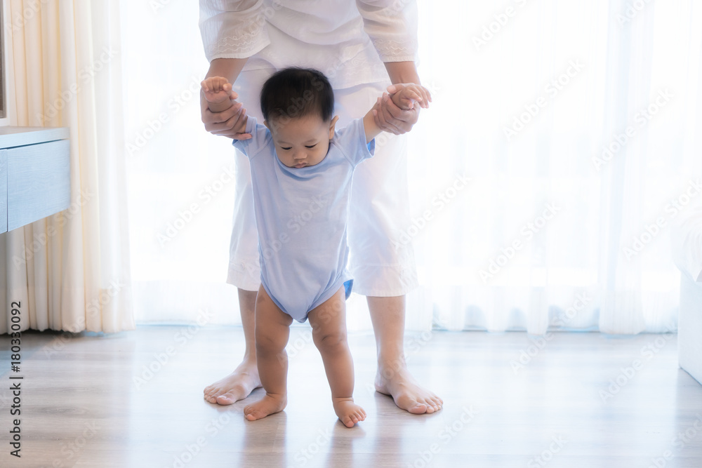 快乐的亚洲小男婴在家里的卧室里与母亲一起学习走路。家人，孩子，chi