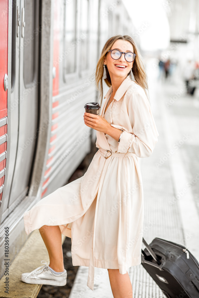 年轻漂亮的女人带着咖啡杯和行李在火车站上车