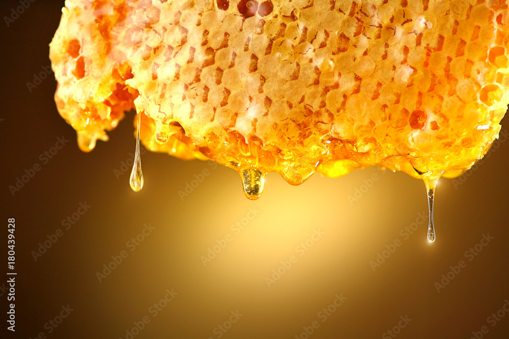 蜂蜜从黄色背景的蜂巢中滴落。厚厚的蜂蜜