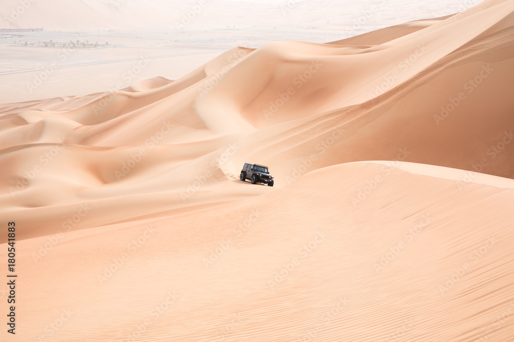 一辆黑色汽车在阿联酋阿布扎比的空旷地带攀登巨大的沙丘。