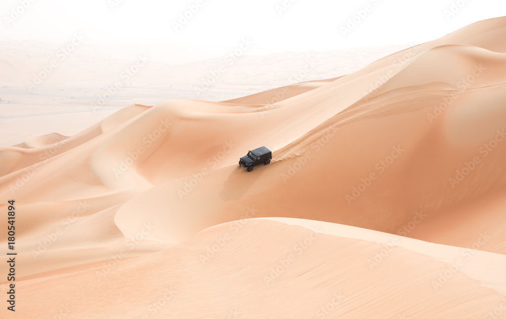 一辆黑色汽车在阿联酋阿布扎比的空旷地带攀登巨大的沙丘。