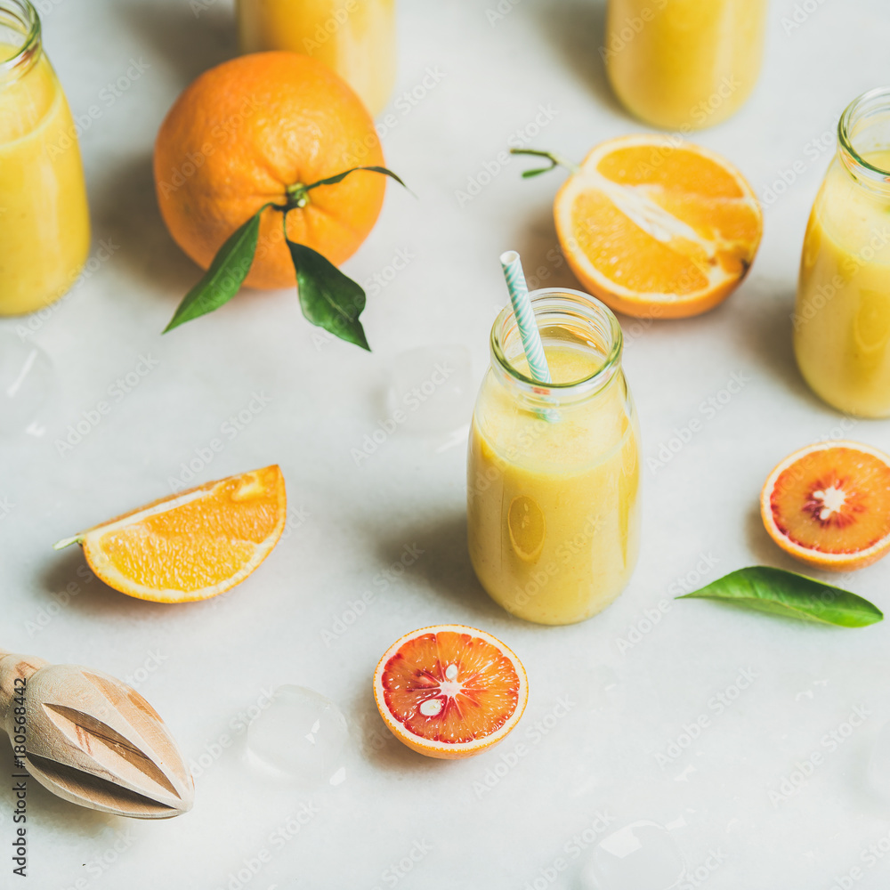 Healthy yellow smoothie with citrus fruit, ginger, ice in glass bottles over light marble table back