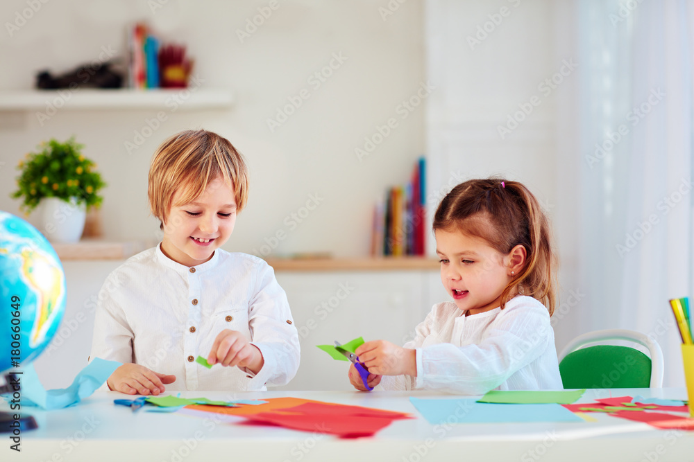 可爱快乐的孩子，桌子上的男孩和女孩剪刀彩色纸工艺品