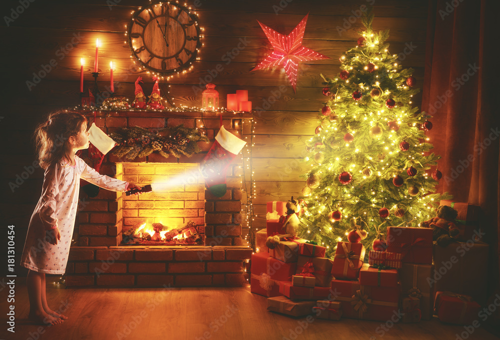 圣诞夜。女婴晚上拿着手电筒在圣诞树下寻找礼物