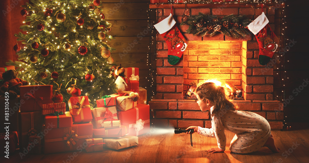 圣诞夜。一个女婴晚上拿着手电筒在圣诞树下寻找礼物