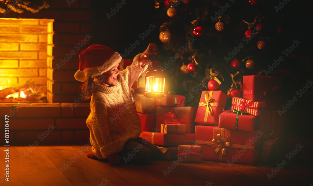 圣诞夜。一个拿着手电筒的小女孩晚上在圣诞树下寻找礼物