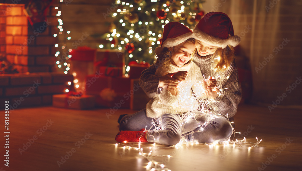 圣诞快乐！母亲和孩子的女儿在树旁戴着发光的花环