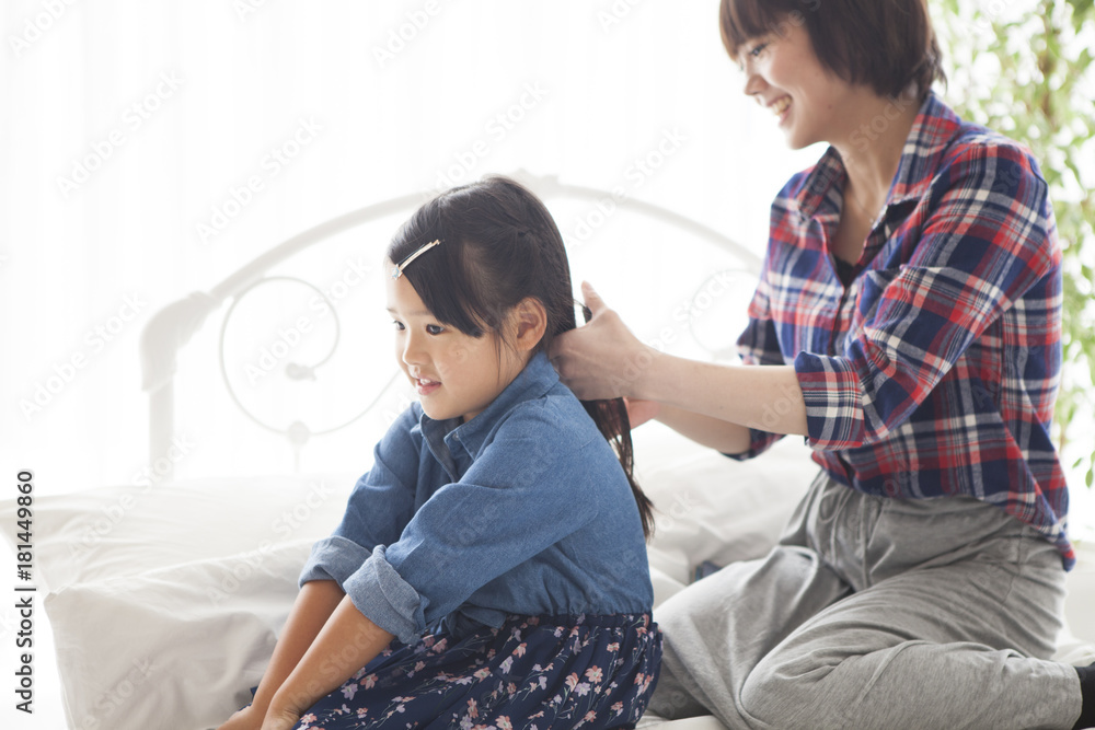 In the bedroom, a young mother is tying her daughters hair.