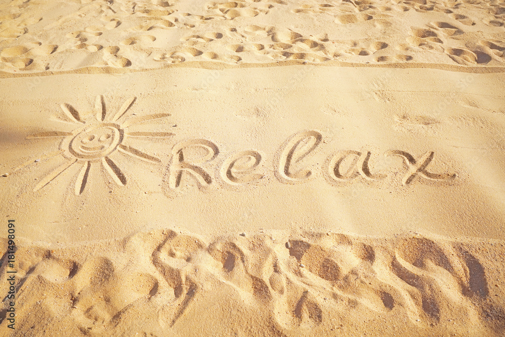 在阳光明媚的沙滩上，在金色的沙滩上画下太阳、痕迹和文字放松的图画。概念