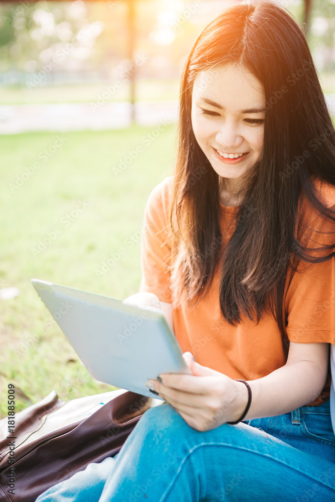 一个年轻或十几岁的亚洲女学生在大学里微笑着看书，看着平板电脑